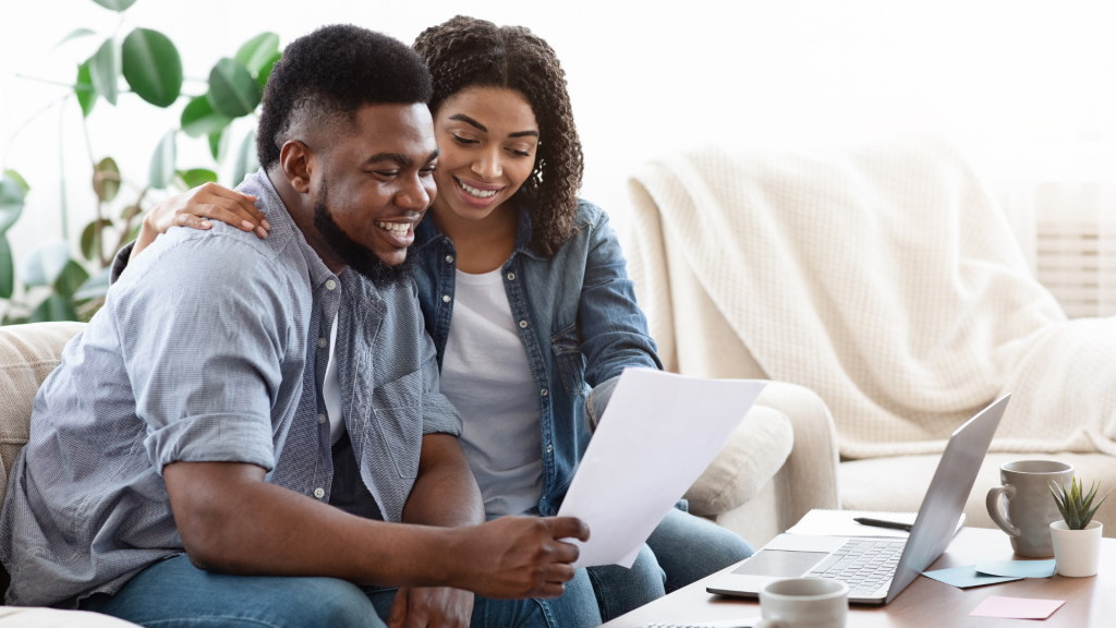 couple sitting on a couch reviewing finances with a laptop and paperwork